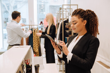 Young cute latin woman working with tablet in clothing store