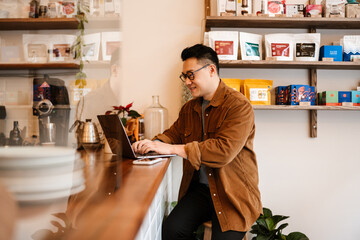 Adult asian man wearing eyeglasses smiling and using laptop in cafe - Powered by Adobe