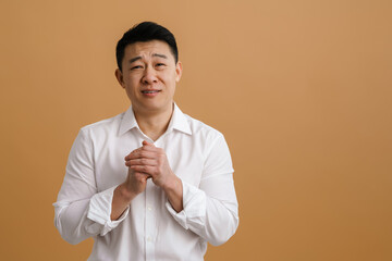 Brunette adult asian man frowning and standing with praying hands