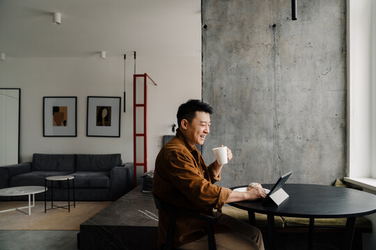 Asian man using tablet computer while having breakfast in kitchen
