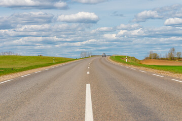 Cars asphalt road through the green agricultural fields background on a sunny summer day.