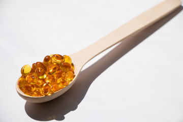 Fish oil pills lie in a wooden spoon on an isolated background, vitamins and supplements