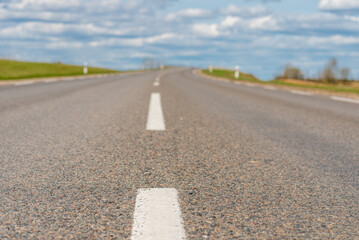 An empty asphalt road through the green agricultural fields with a forest in the background on a sunny summer day.