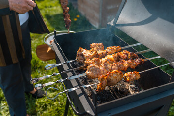 Senior woman doing process of cooking barbecue completed on a metal grill.Cooking for a picnic.Delicious, juicy, aromatic pieces of shashlik.Meadow background.