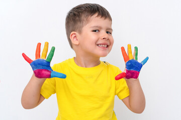 A 4-year-old brunette boy in a yellow T-shirt with painted multicolor rainbow-colored palms on a white background. The concept of advertising for the school of drawing, both online and offline.
