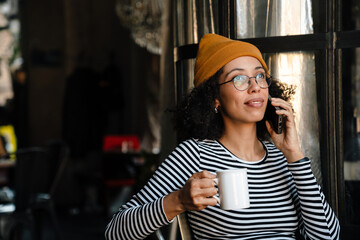 Young african american woman drinking tea and using cellphone in cafe