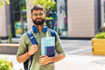 indian student with blue headset and backpack holding books at sunny day
