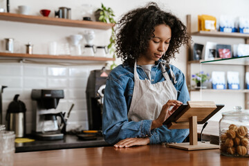 Black barista woman wearing apron working with tablet computer in cafe