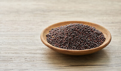 black mustard seed in wood plate on wooden table background. a pile of black mustard seed in wood plate on wooden table background.        
