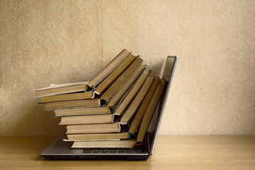 Opened books is on the laptop. Still life of items for reading. Stack of books with laptop on table in classroom.