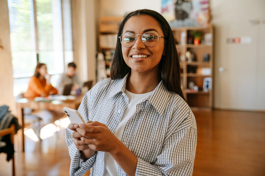 Black woman smiling and using mobile phone while working in office