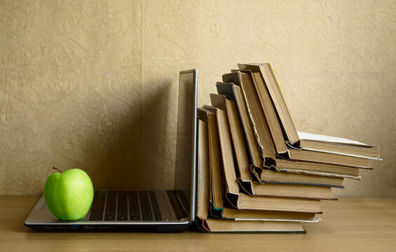Opened books is on the laptop. Still life of items for reading. Stack of books with laptop on table in classroom. back to school idea. Audio books concept. green apple fruit.