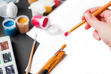 Person holding brush dipped in red paint over white paper ready for drawing