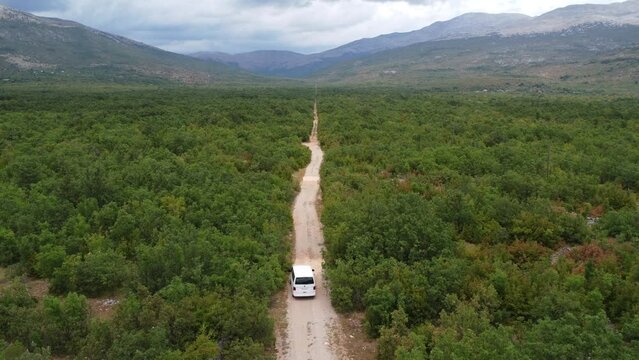 a white van drives on a straight gravel road in the densely forested area of the croatian dinara mountains, flimed with the drone