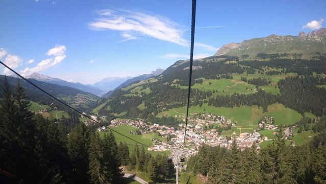 Cable car ride in the canton of Grisons. The gondola lift descends into the valley. You can see the small village in the valley. You can see the beautiful nature in Switzerland