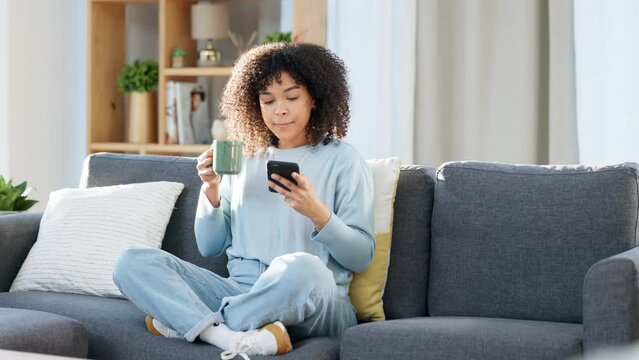 Woman reading a text message on a phone, scrolling on social media online or browsing an app while drinking coffee at home. One happy, smiling and comfy black female searching the web with tea