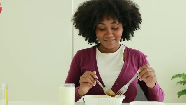 Portrait african american teenage girl drinking milk while eating rice and fried eggs in a plastic container bought at the supermarket with spoonful of rice. Show how happy she is.