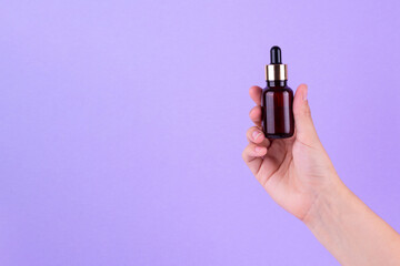 Serum bottle in female hands, top view. Transparent moisturizer for skin care. Nourishing essential...