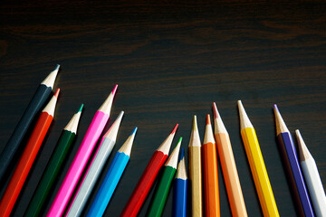 暗い木の机の上の沢山の綺麗な色鉛筆
