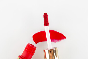 drop of red liquid lipstick smeared on a white background. Red lip gloss in a tube with an applicator isolated on a white background - obrazy, fototapety, plakaty