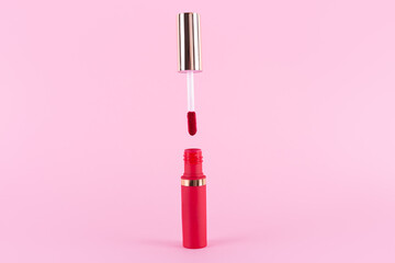 Lipstick and applicator wand on pastel pink background. Liquid lip stick red lip gloss open tube. Makeup cosmetic product. Top view, flat lay, copy space - obrazy, fototapety, plakaty