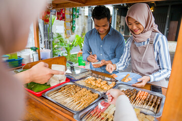muslim couple ordering food to break fasting in traditional food market stall served by the seller