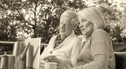 Elderly people living their life at its best. Couple of retired people making breakfast outdoor and using laptop.