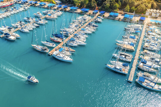 Aerial view of luxure yachts and motorboats moored in a port with clear blue water in summer. Pula, Croatia. Top view from drone of sailboats and various speed boats in dock