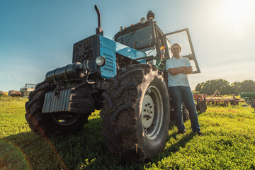 Farmer stands by tractor in agricultural fields and land. Farming, growing vegetables and fruits, harvesting. © DedMityay