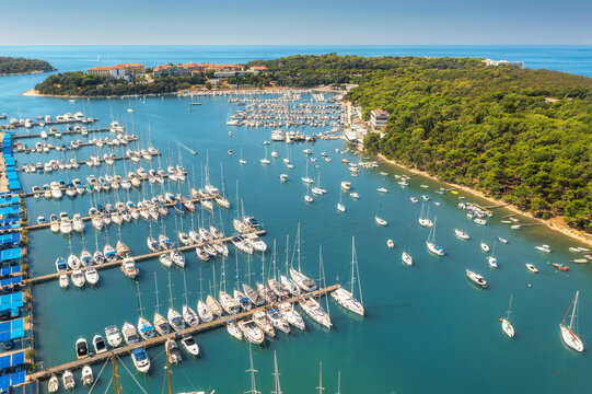 Aerial view of luxure yachts and motorboats moored in a port with clear blue water in summer. Pula, Croatia. Top view from drone of sailboats and various speed boats in dock