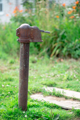 Am old red metal russian water pump on the street against blurry grass background. Wooden pallet is under it
