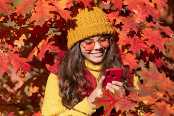 happy kid in sunglasses messaging on smartphone at autumn leaves on natural background