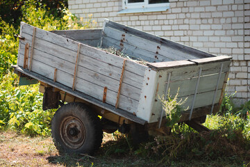 An old abandoned wheelbarrow in the grass near a brick white house against a bright blurry grass on the background