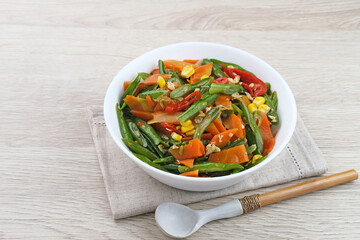 Orak arik sayur or stir fried vegetables with carrot, bean, corn and egg. Served in white bowl on wooden background. 