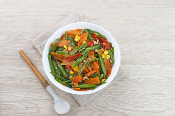 Orak arik sayur or stir fried vegetables with carrot, bean, corn and egg. Served in white bowl on wooden background. 