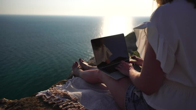 Successful Business Woman In Yellow Hat Working On Laptop By The Sea At Sunset Time. Pretty Lady Typing On Computer At Summer Day Outdoors. Freelance, Digital Nomad, Travel And Holidays Concept.