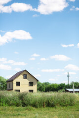 A beige house in the distance on the field with a tall grass and trees on the background with a electrical pole. Nice blue cloudy clean sky is above