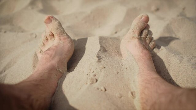 Man feets on beach in warm sand. Haired legs funny moving fingers. Male sunbathing on ocean resort. Freedom lifestyle and traveling in holiday concept