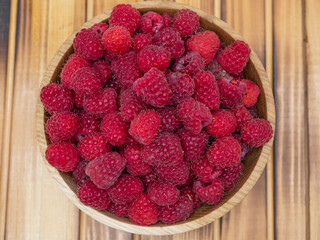 Fresh raspberries in wooden bowl on wooden background. Top view
