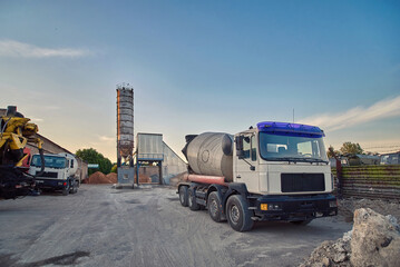 Concrete batching and manufacture plant, parked mixer trucks at the plant yard, ready to deliver concrete products. Ready-mix concrete plant. Construction industry concept.