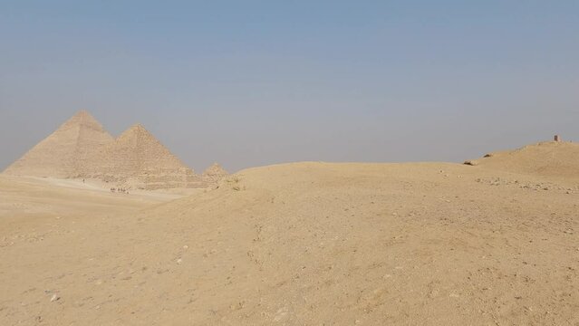Panning view of Pyramid complex with tourists visiting in a immersive blue sky. Egypt
