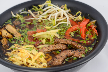 Korean dish soup with noodles, meat and soybean sprouts in a black plate, macro photo
