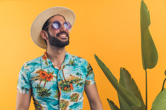 Young hispanic man with beard wearing sunglasses summer clothes standing next to big plant looking forward to traveling. Tourist. Studio shot. High quality photo