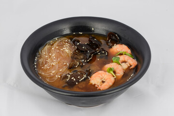 Korean dish soup with mushroom noodles and shrimp in a black plate
