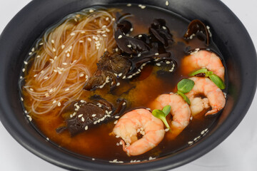 Korean dish soup with noodles, mushrooms and shrimp in a black plate, macro photo
