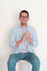 Adult Asian man give applause while sitting in a bench