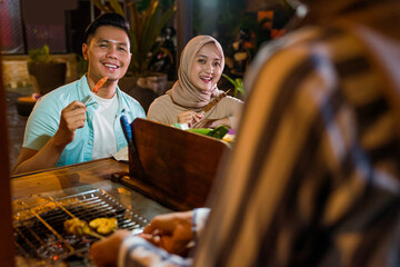 muslim couple ordering food to break fasting in traditional food market stall served by the seller