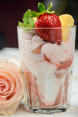 strawberry tiramisu dessert in a glass decorated with strawberries and a mint leaf on a background with a flower
