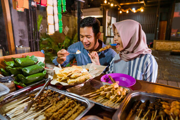happy beautiful muslim couple enjoying having dinner out at traditional food market in the evening during ramadan