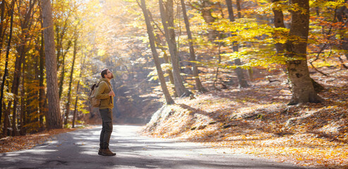 Young handsome man posing in autumn forest. young hipster guy with backpack , traveller standing in woods, Hiking, Forest, Journey, active healthy lifestyle, adventure, vacation concept.